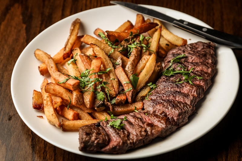 Corte de carne grelhada fatiada servida com batatas em prato branco