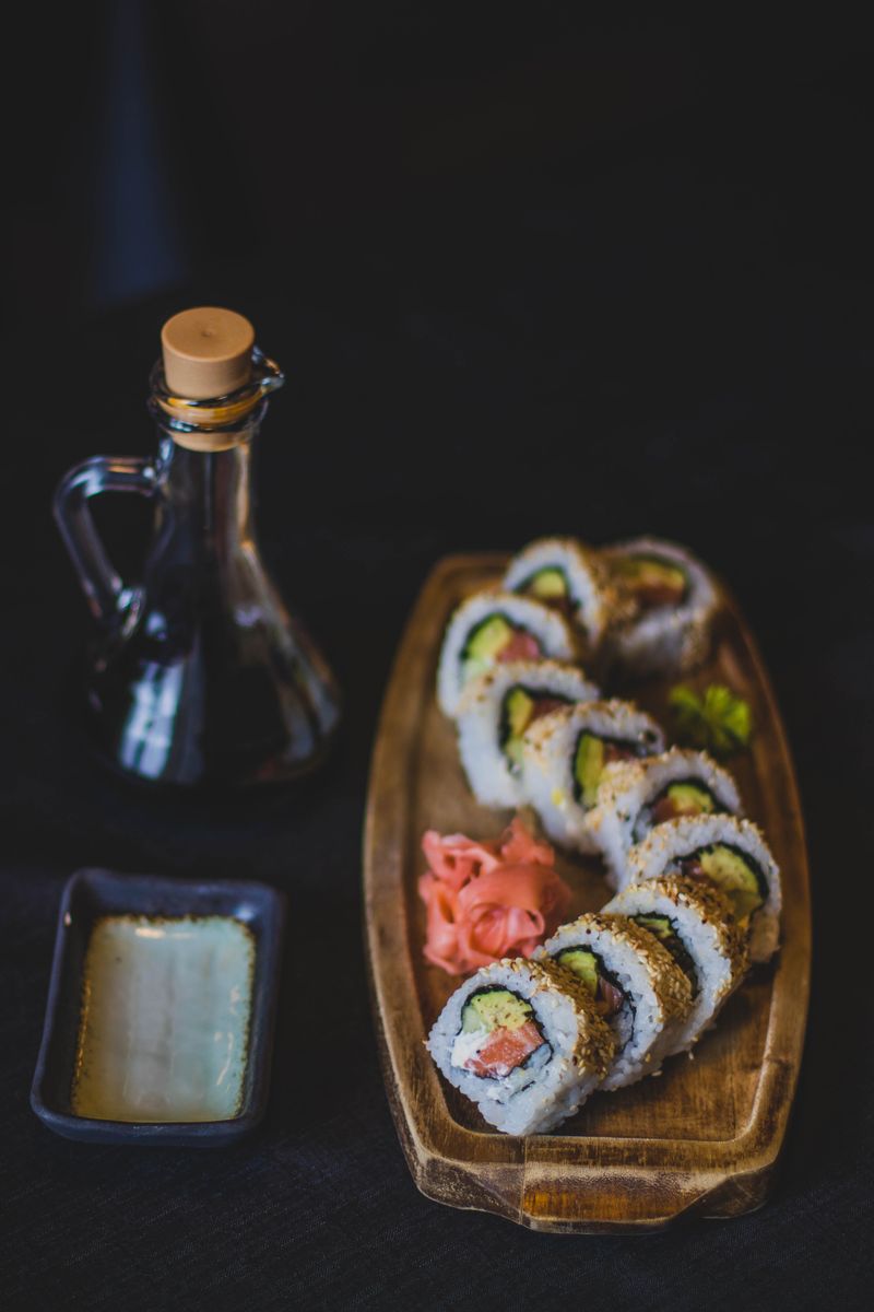 Tábua de madeira com peças de sushi e molhos sobre fundo escuro
