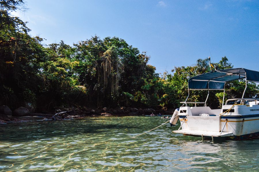 Embarcação ancorada em água transparente junto à mata atlântica em Paraty