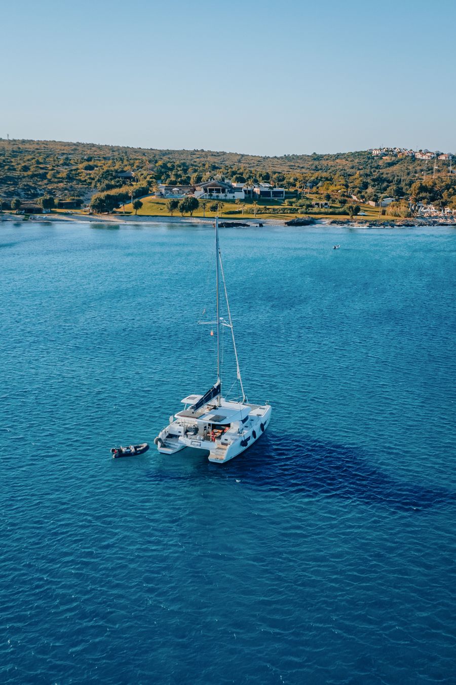 Catamarã ancorado em enseada de água azul profunda vista de cima